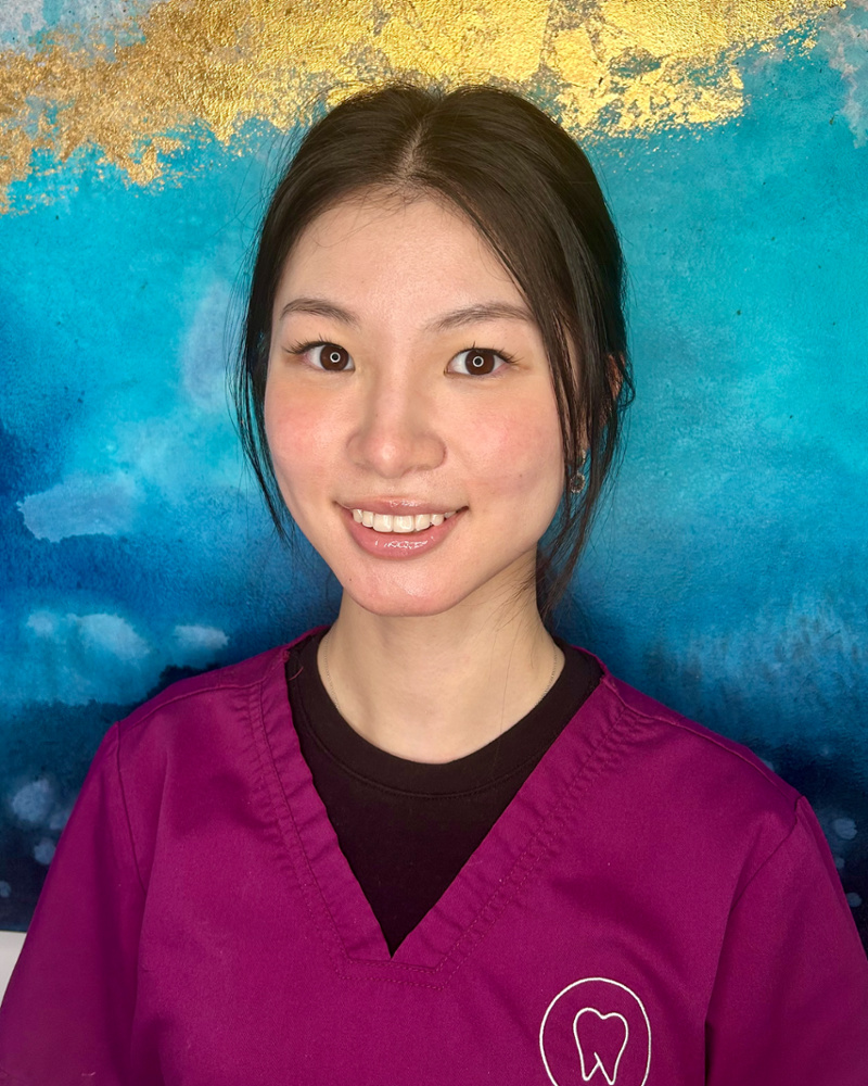 Ruth Wong, Oral Health Therapist, smiling warmly in purple dental uniform with tooth logo